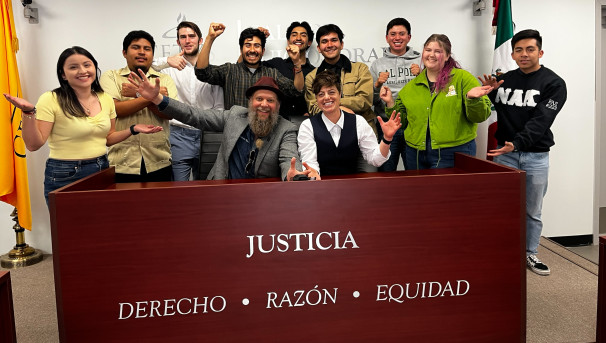 Various debate team members cheering behind a booth labeled "Justicia"