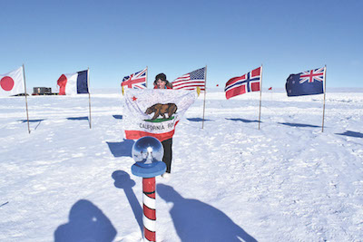 Lesley Anderson holds the California state flag signed by her students at the ceremonial South Pole marker.