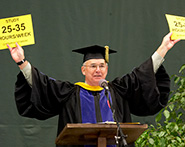 Phil Bailey in Commencement regalia holds Study 25-35 signs