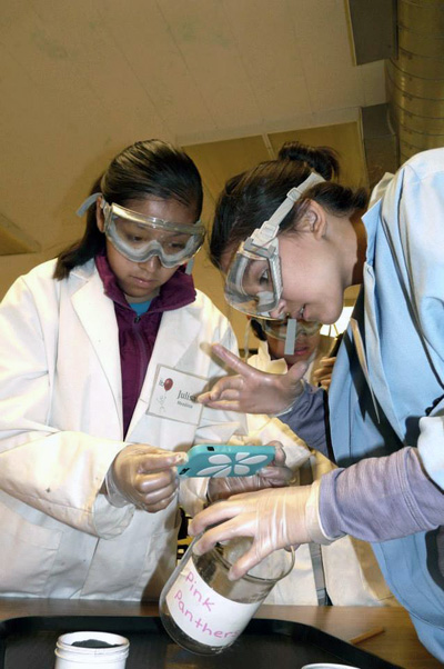 Two female students taking a picture of a beaker.