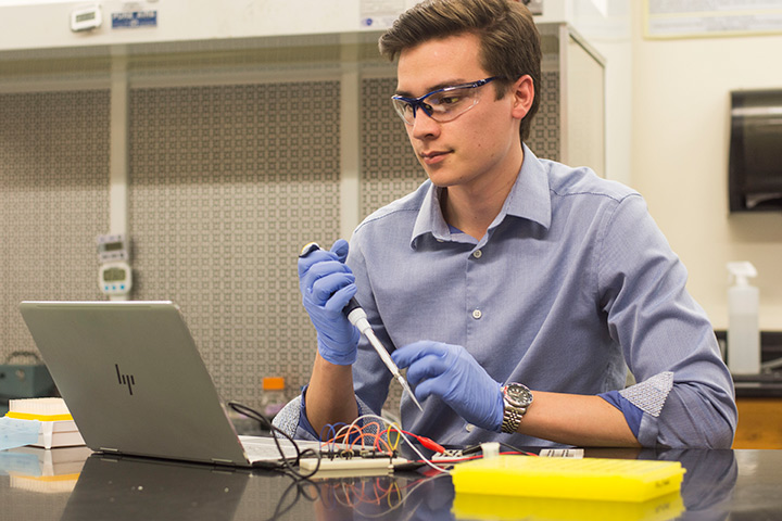 Brandon Strong analyzes experimental results in the lab holding pipette and looking at computer