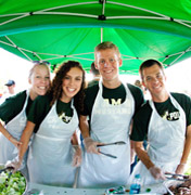 Cal Poly students under green umbrella serving food