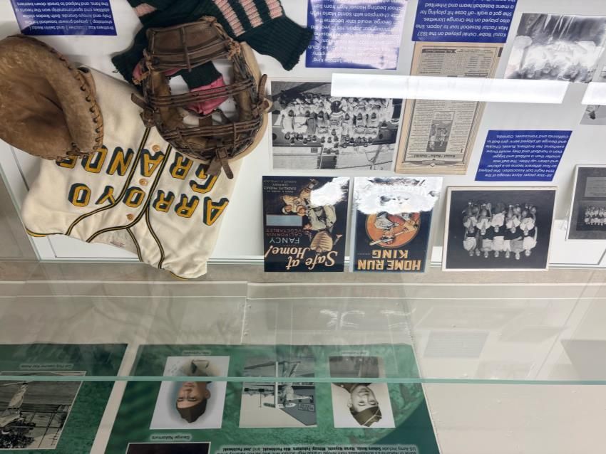 A display at the "Through a Diamond" exhibit, containing photographs, an old jersey, and an old baseball glove.