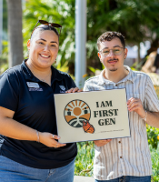 Two people holding up a sign that says "I Am First Gen"