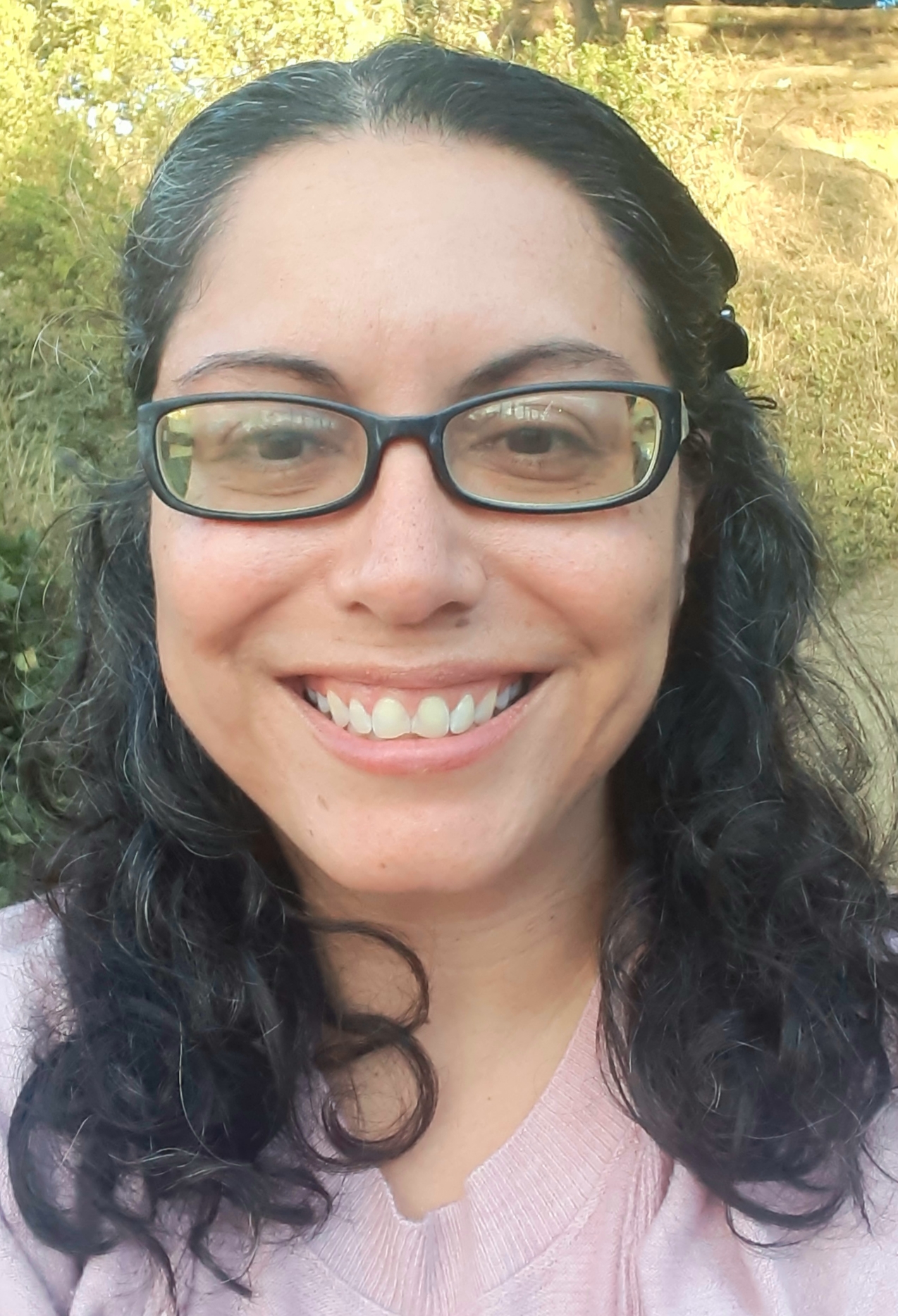 Photo of smiling woman with glasses, black and gray wavy hair and dark brown eyes. 