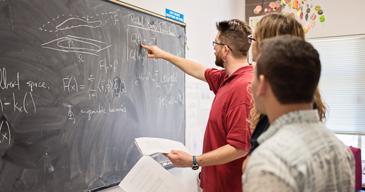 Faculty working with students at chalkboard.