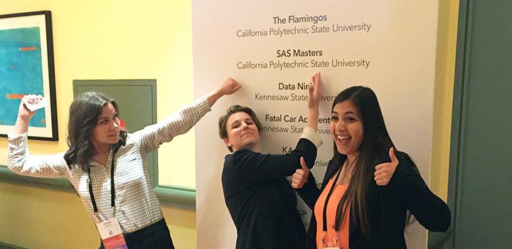 Students strike silly poses in front of competition sign with their team name on it.