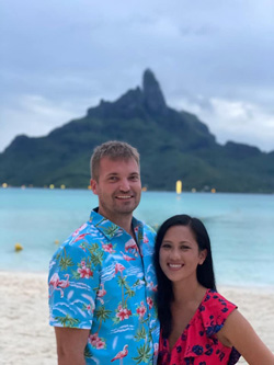 Aaron Hardiek and his partner at the beach with a large island in the background