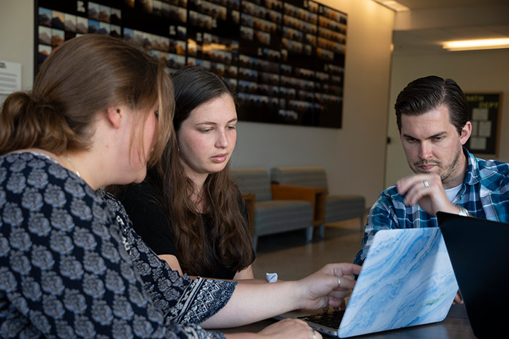 Two professors and a student looking at a computer screen together.