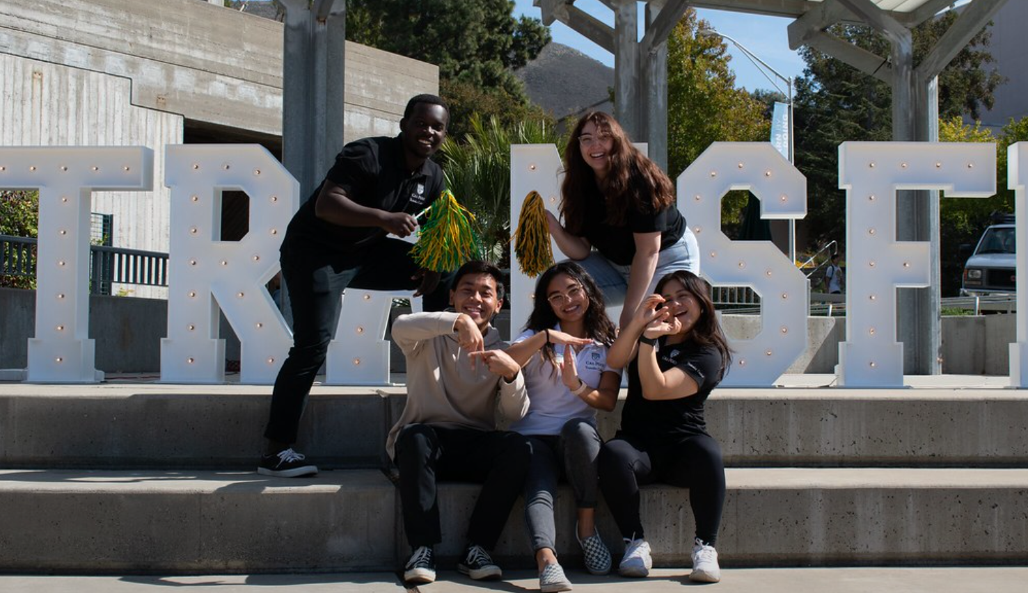 5 students smiling in front of marquee letters spelling transfer