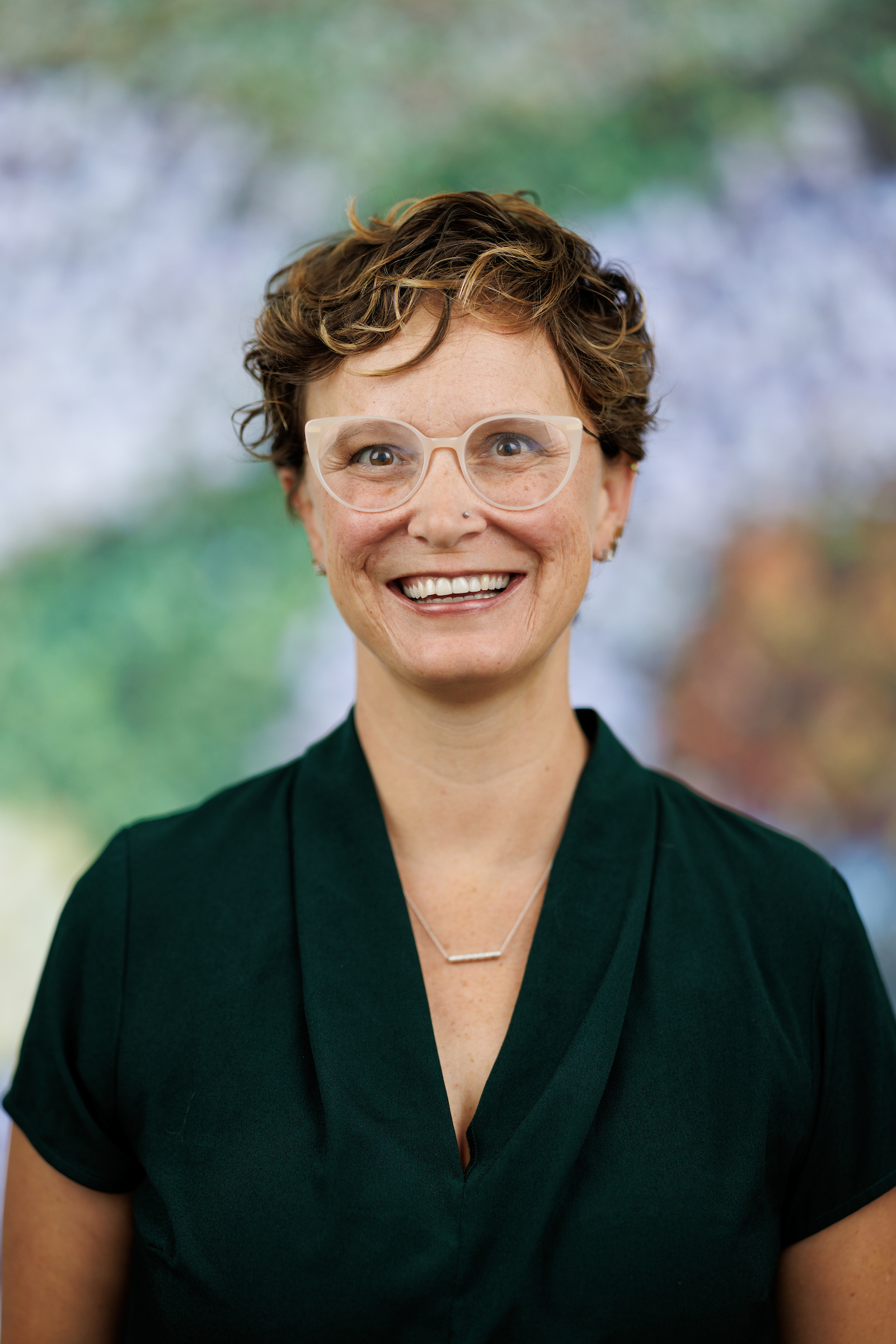 A headshot of Didi Hawkins who has short brown hair, glasses, and is wearing a green shirt.
